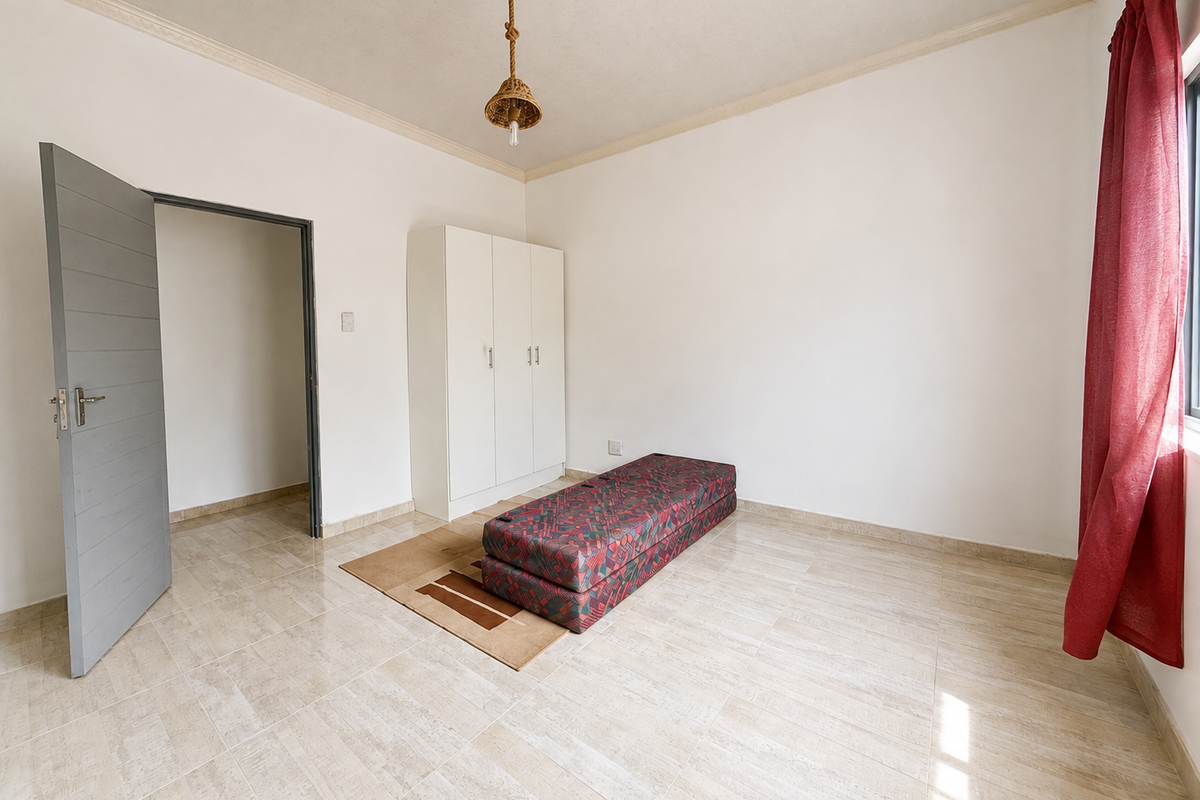 A simple, well-lit bedroom featuring neutral tiled flooring, a built-in wardrobe, and a coved ceiling, offering a clean and functional space.