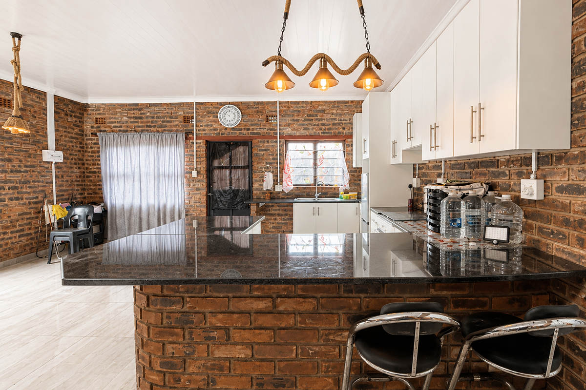 A spacious kitchen featuring exposed brick walls, granite countertops, white cabinetry, and a breakfast bar, offering a rustic yet functional cooking and dining space.