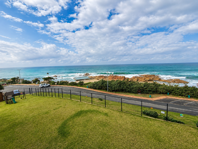 A scenic elevated view overlooking the coastline, featuring a well-maintained lawn, perimeter fencing, and direct views of the ocean and rocky shore.