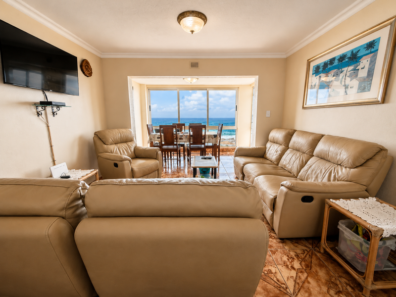 Open-plan living and dining area featuring tiled floors, neutral walls, and large sliding doors offering expansive ocean views.