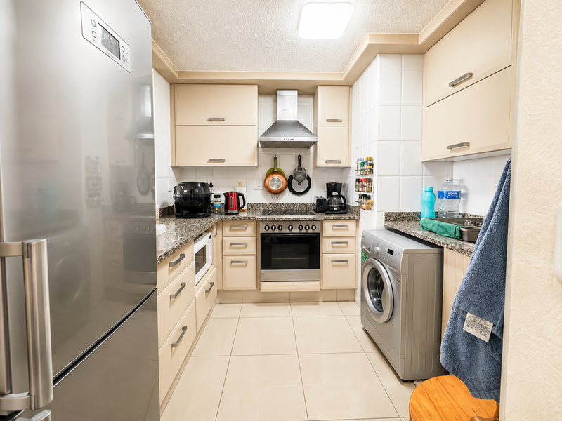 A compact, functional kitchen featuring light-toned cabinetry, granite countertops, a built-in oven with extractor fan, and integrated laundry facilities.