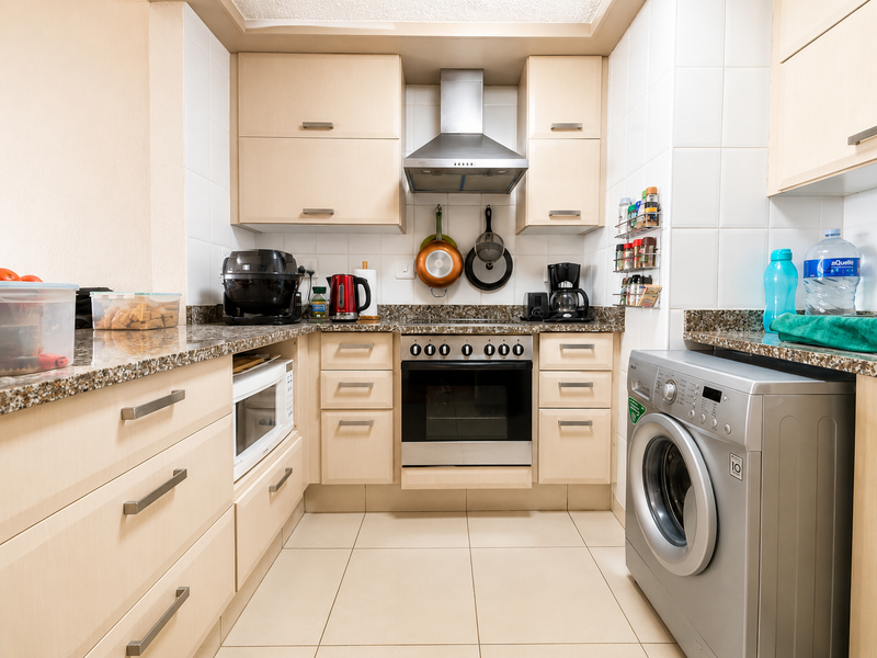 A functional kitchen featuring light wood cabinetry, granite countertops, a built-in oven with extractor fan, and integrated laundry facilities.