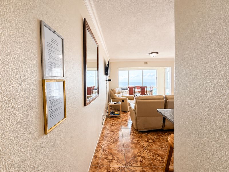 A view from a hallway looking into an open-plan living and dining area with tiled floors and large windows overlooking the ocean.