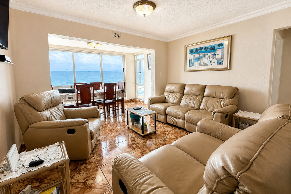 A spacious living room featuring ceramic tiled flooring, coving, and large sliding glass doors that provide expansive ocean views.