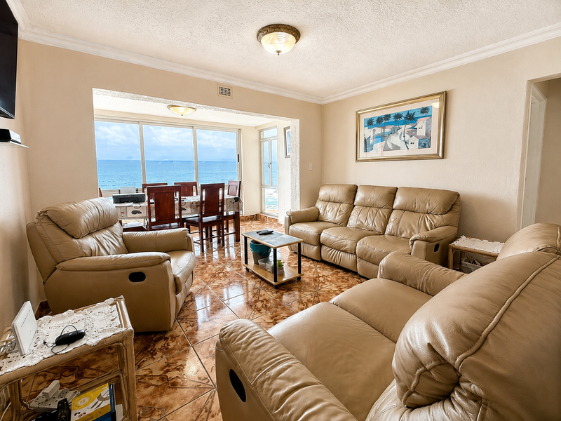A spacious living room featuring ceramic tiled flooring, coving, and large sliding glass doors that provide expansive ocean views.