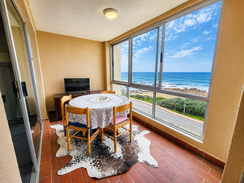Enclosed balcony featuring terracotta tile flooring and expansive sliding glass windows offering panoramic ocean and coastal views.