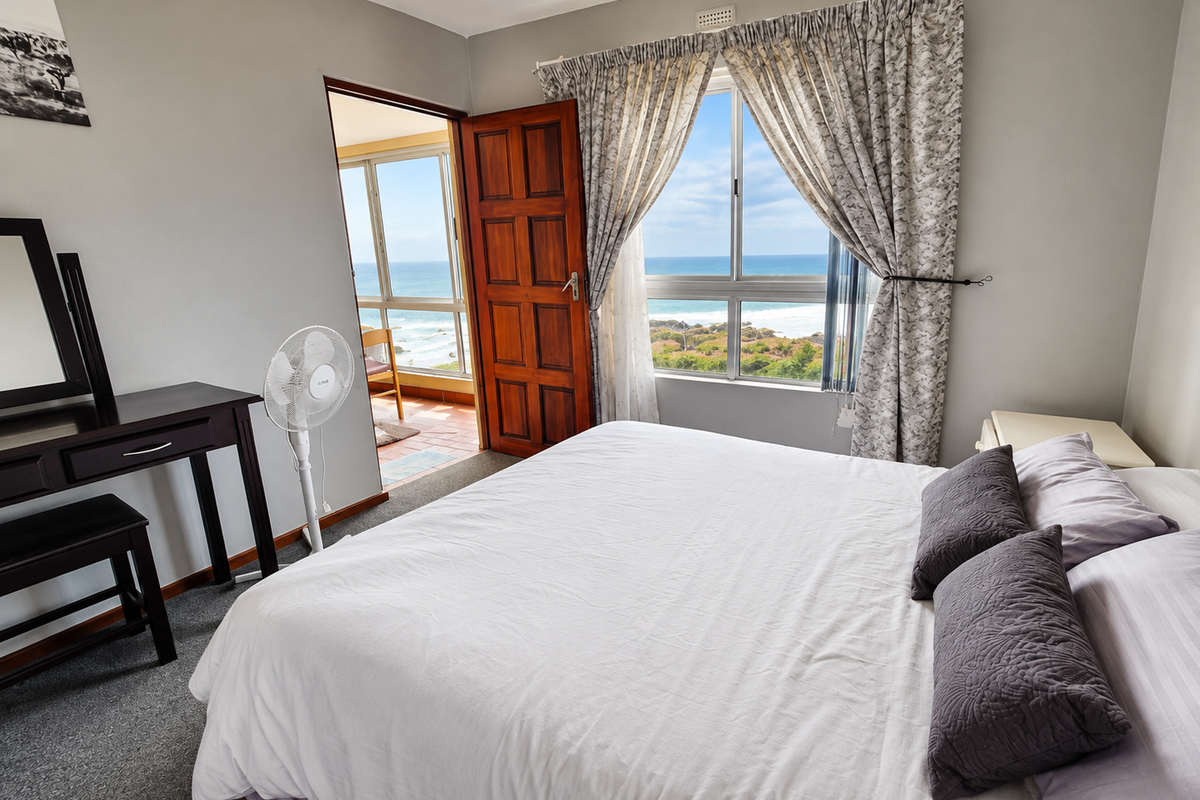 A bedroom featuring carpet flooring, a timber door, and a window with ocean views, providing access to an adjoining balcony area.