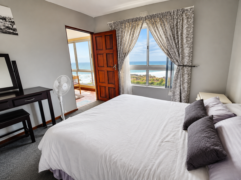 A bedroom featuring carpet flooring, a timber door, and a window with ocean views, providing access to an adjoining balcony area.