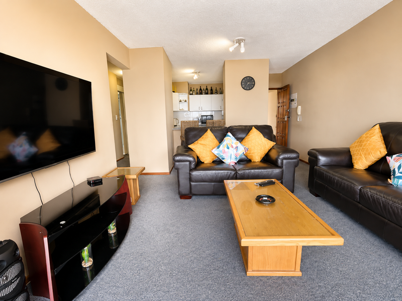Open plan living area featuring a carpeted lounge space flowing into a compact kitchen with built-in cabinetry.