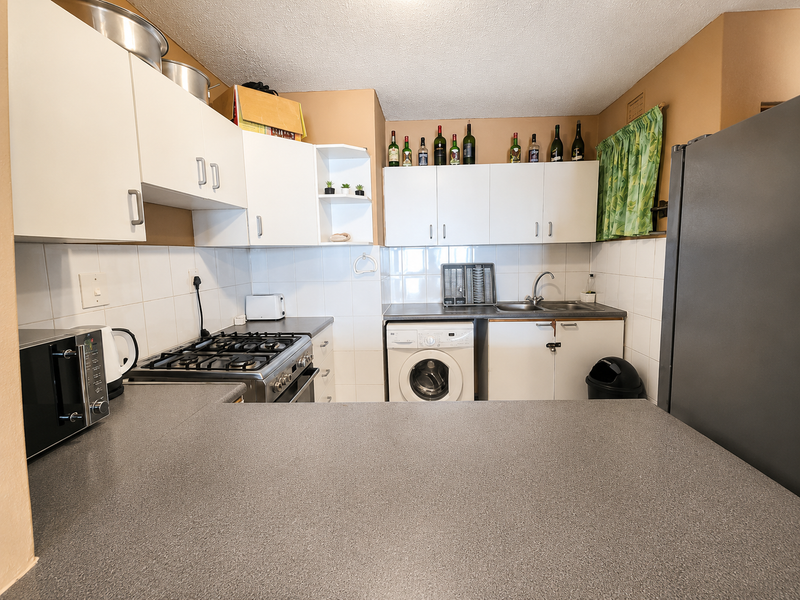 Functional kitchen featuring white cabinetry, gas hob, oven, integrated washing machine, and tiled backsplash with ample countertop workspace.