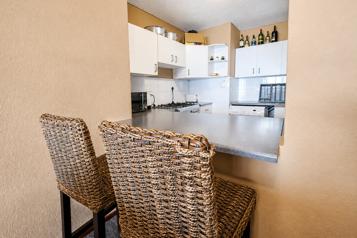 A compact kitchen featuring white cabinetry, a dark laminate breakfast bar, and a gas hob, viewed from the adjacent living area.