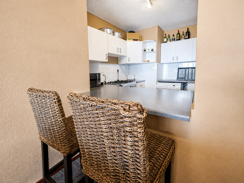 A compact kitchen featuring white cabinetry, a dark laminate breakfast bar, and a gas hob, viewed from the adjacent living area.
