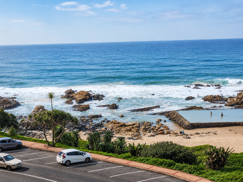 A scenic elevated view of the ocean, rocky coastline, and a natural tidal pool, showcasing the property's prime coastal location.