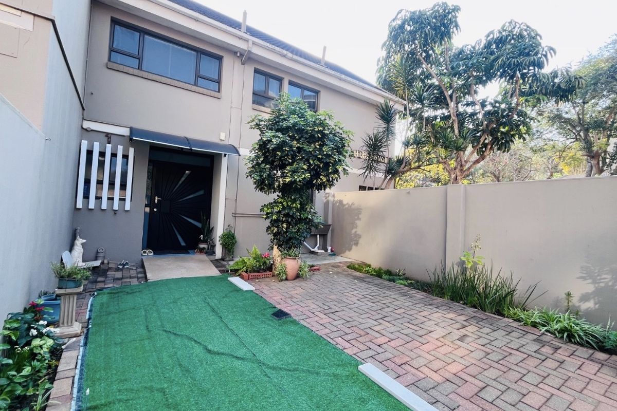 Rear exterior view of the townhouse featuring a paved courtyard area, boundary wall, and direct access to the main entrance.