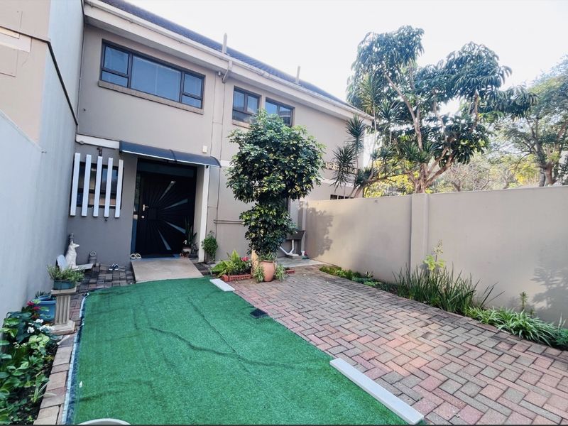 Rear exterior view of the townhouse featuring a paved courtyard area, boundary wall, and direct access to the main entrance.