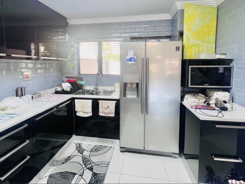 Modern kitchen featuring glossy black cabinetry, white stone countertops, subway tile backsplash, and integrated microwave, offering a clean and functional workspace.