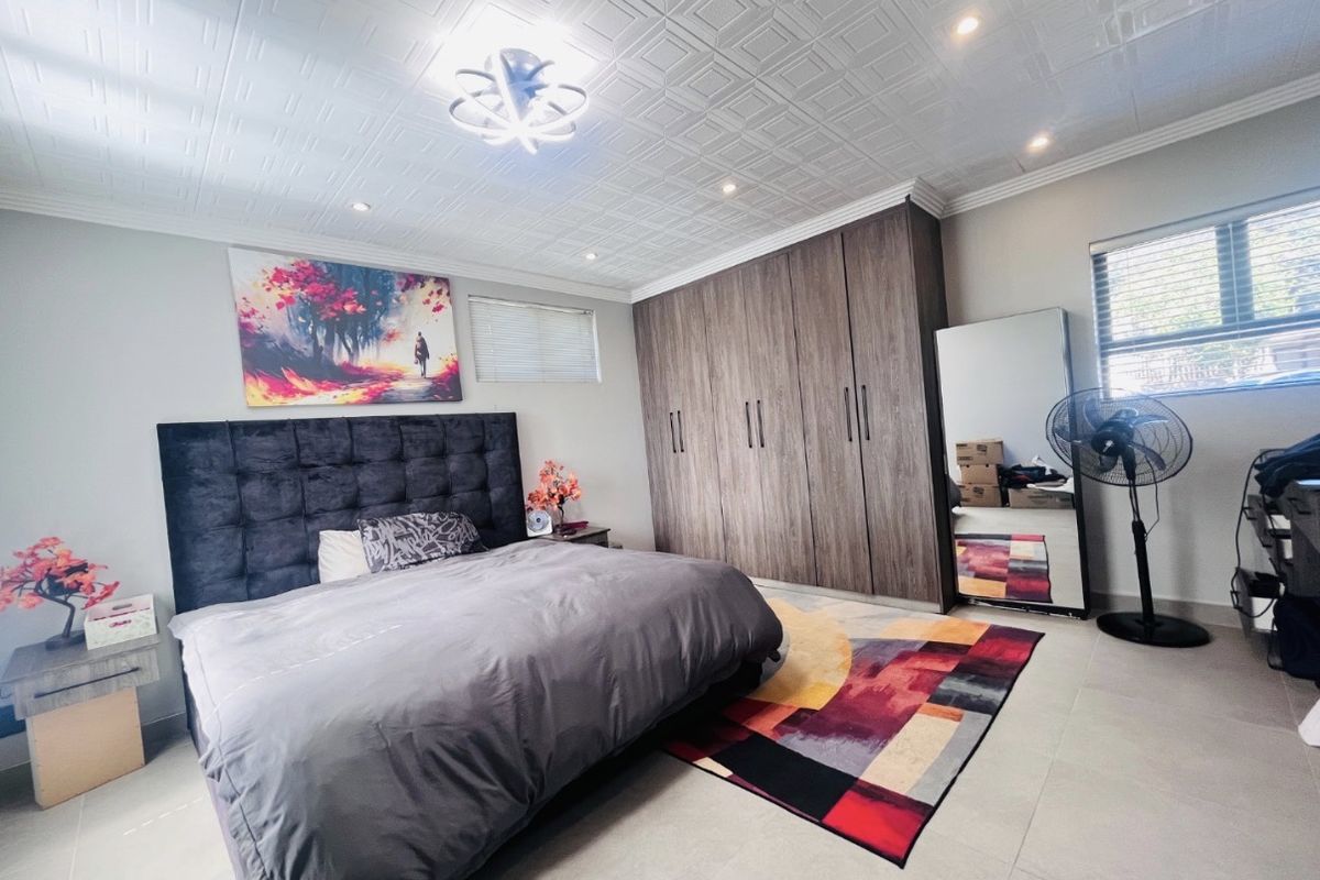 Spacious bedroom featuring built-in wooden cupboards, tiled flooring, and a decorative textured ceiling with integrated recessed lighting.
