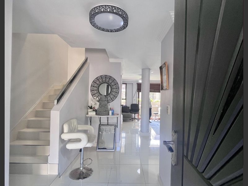 A bright entrance hall featuring polished tiled flooring, a modern staircase with a handrail, and an open-plan layout leading into the living area.