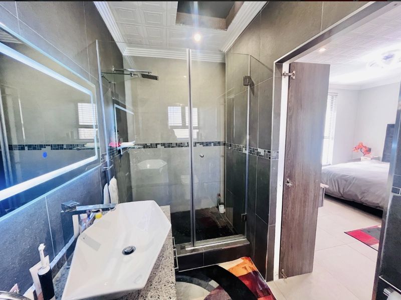 Modern bathroom featuring a glass-enclosed shower with rain shower head, vessel sink on a granite vanity, and contemporary LED backlit mirror.