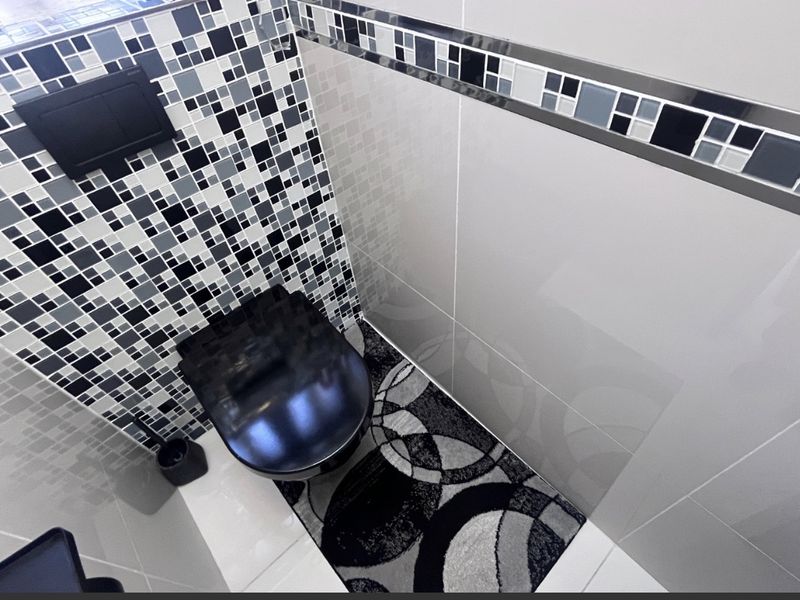 A modern bathroom featuring a wall-mounted toilet, a striking black and white mosaic feature wall, and sleek ceramic tiling.