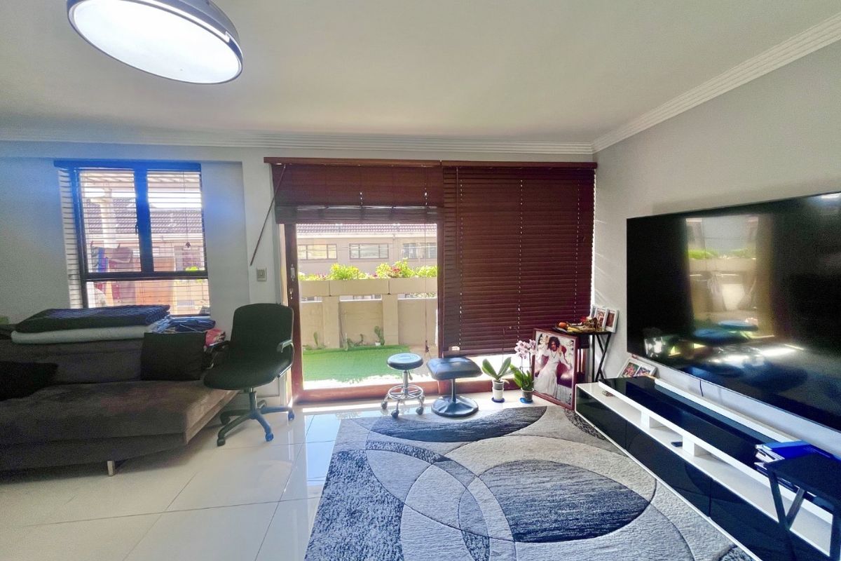 A living room featuring tiled flooring, a sliding glass door leading to a balcony, and venetian blinds.