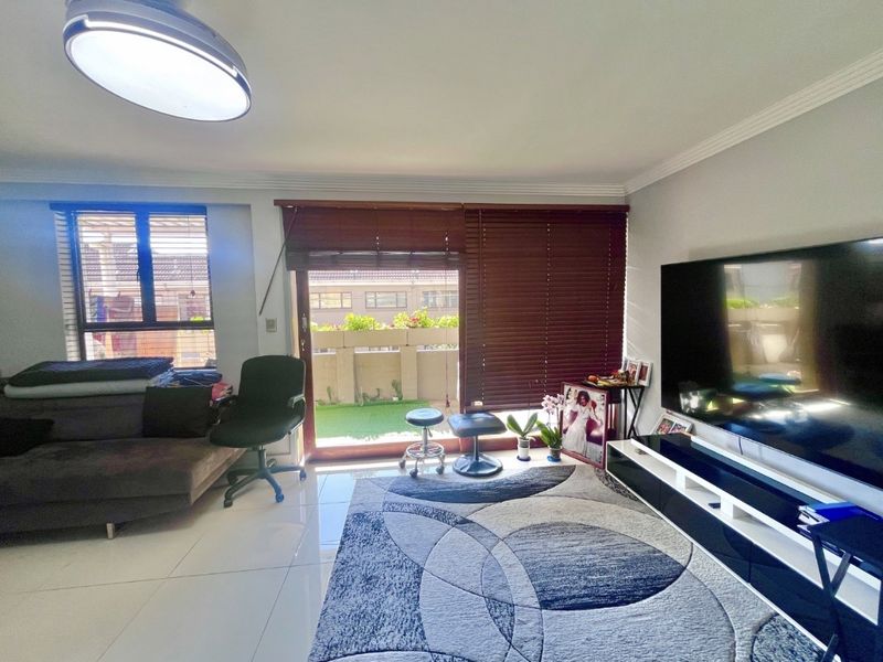 A living room featuring tiled flooring, a sliding glass door leading to a balcony, and venetian blinds.