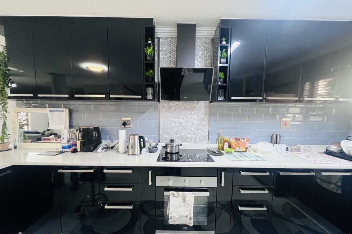 Modern kitchen featuring high-gloss black cabinetry, stone countertops, subway tile backsplash, and integrated stainless steel appliances including an oven and extractor fan.