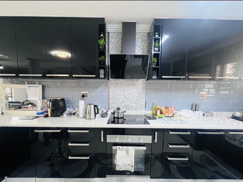 Modern kitchen featuring high-gloss black cabinetry, stone countertops, subway tile backsplash, and integrated stainless steel appliances including an oven and extractor fan.