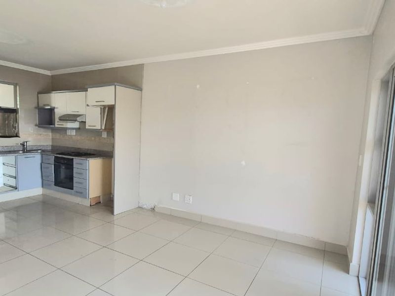 An open-plan living and kitchen area featuring tiled flooring, built-in cabinetry with an integrated oven and hob, and access to an outdoor space.