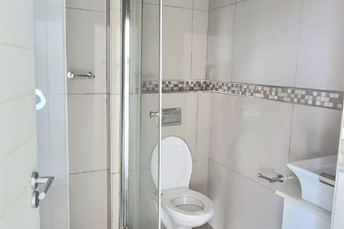 A clean, modern bathroom featuring a glass-enclosed shower, wall-mounted toilet, and a vanity basin with neutral tiled finishes.