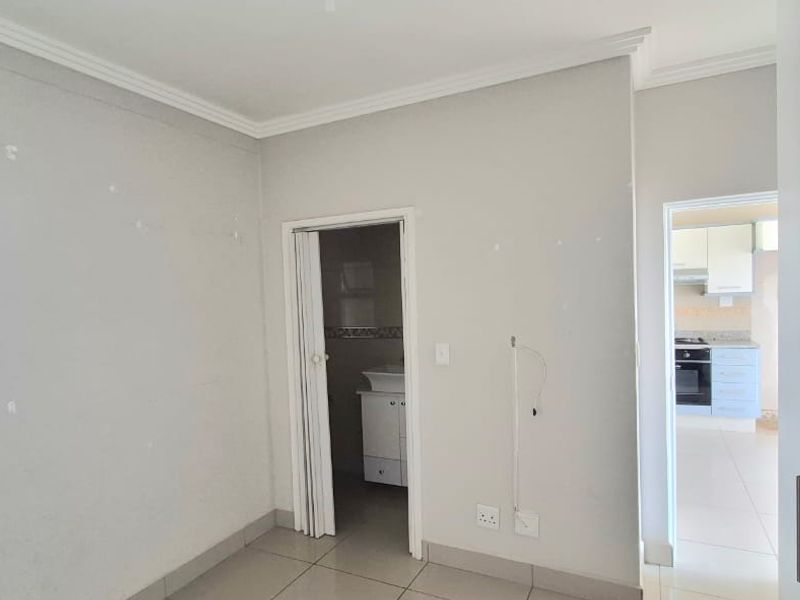 An empty bedroom featuring tiled flooring, built-in cupboards, and direct access to an en-suite bathroom, with a view into the adjacent kitchen area.