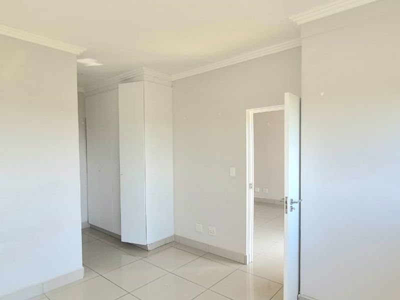 A bright, empty bedroom featuring neutral tiled flooring, built-in cupboards, and classic cornicing, offering a clean canvas for personalization.