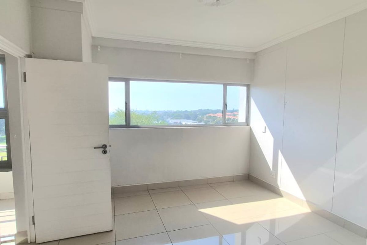 A bright, empty bedroom featuring tiled flooring, built-in cupboards, and large windows offering natural light and an elevated view.