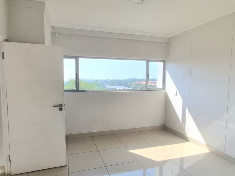 A bright, empty bedroom featuring tiled flooring, built-in cupboards, and large windows offering natural light and an elevated view.