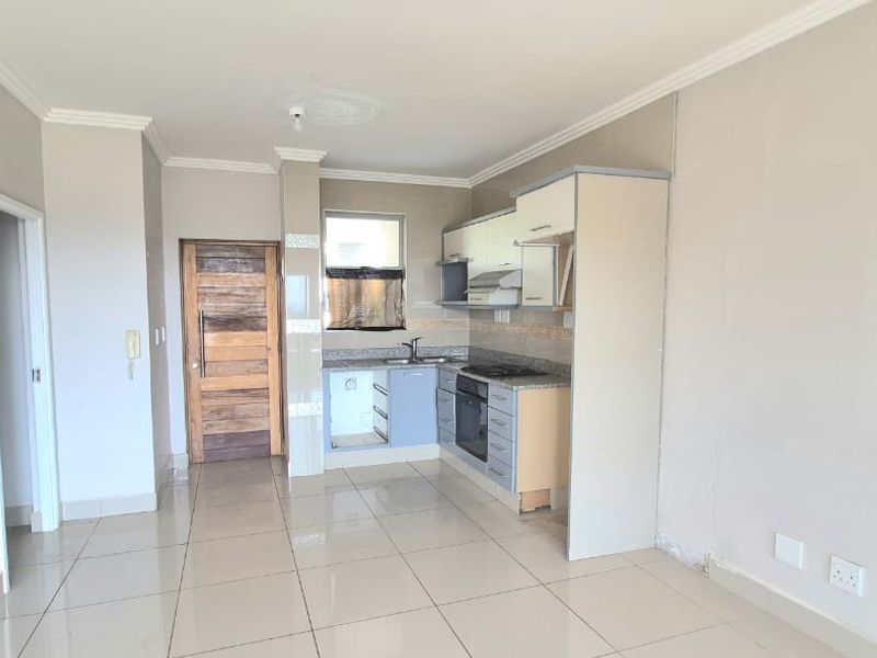 Open plan living area featuring a compact kitchen with built-in cabinetry, granite countertops, and tiled flooring throughout.