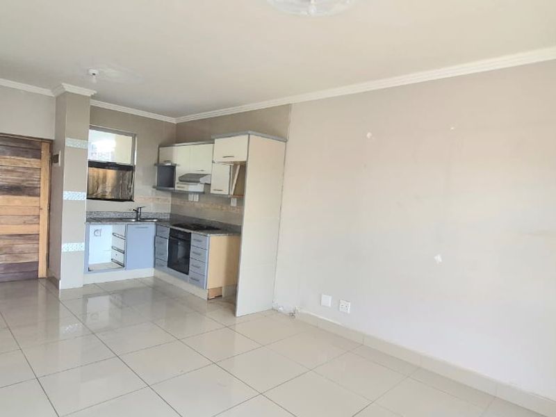 Open plan living area featuring tiled floors and a compact kitchen with built-in cabinetry, oven, and hob.