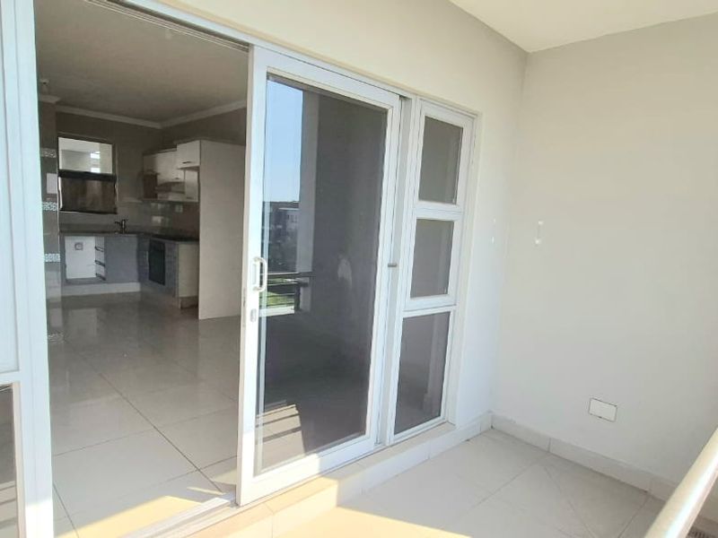 A bright balcony with tiled flooring and a metal balustrade, providing a seamless transition to the open-plan kitchen area through sliding glass doors.