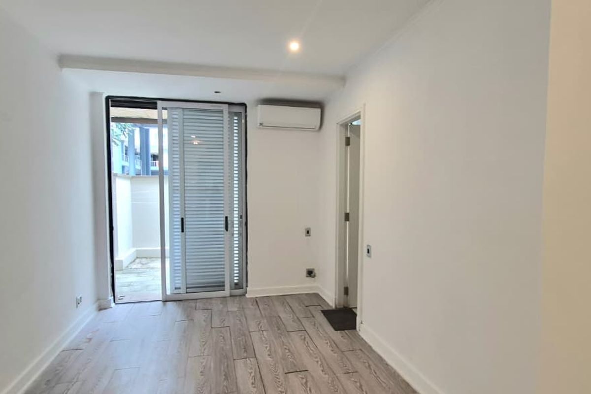 An empty living room featuring wood-look tile flooring, a wall-mounted air conditioning unit, and a sliding glass door leading to an outdoor area.