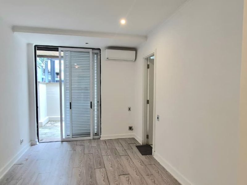 An empty living room featuring wood-look tile flooring, a wall-mounted air conditioning unit, and a sliding glass door leading to an outdoor area.