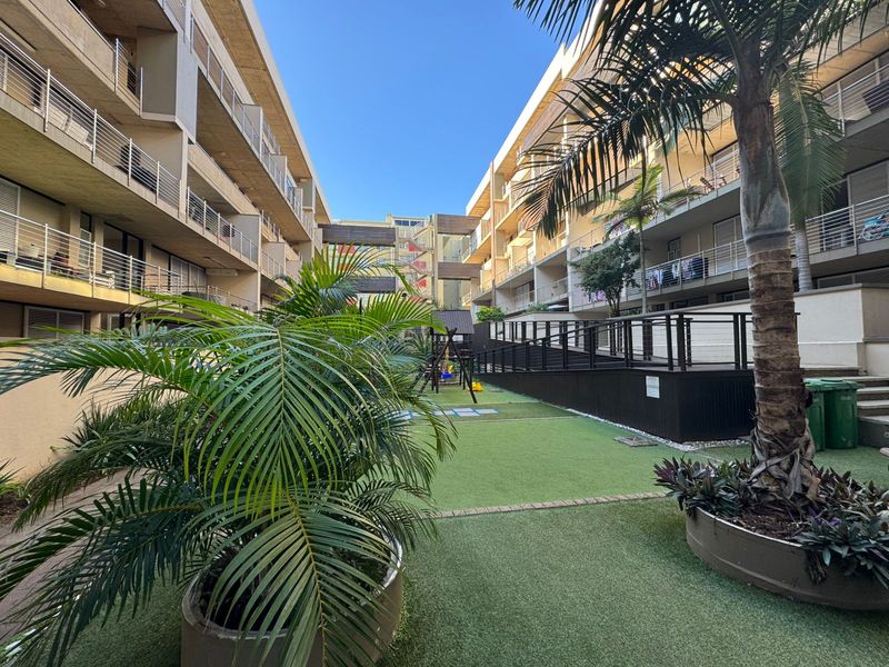 A well-maintained communal courtyard area between apartment blocks featuring artificial turf, landscaped planters, and access to balcony levels.