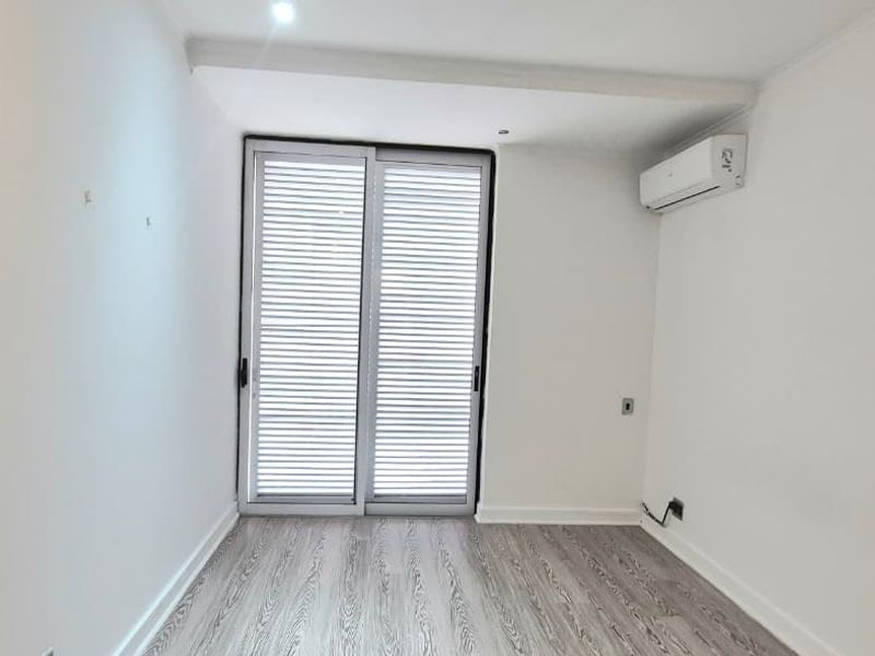 An empty bedroom featuring light-toned laminate flooring, a split-system air conditioner, and a sliding glass door with integrated shutters.