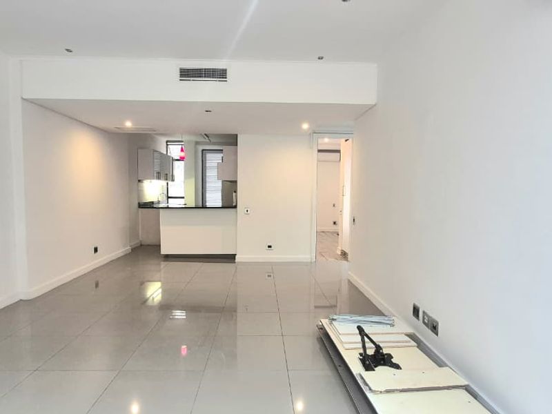 Spacious open-plan living area featuring polished porcelain tiles, recessed lighting, and a modern kitchen with a breakfast bar and integrated cabinetry.