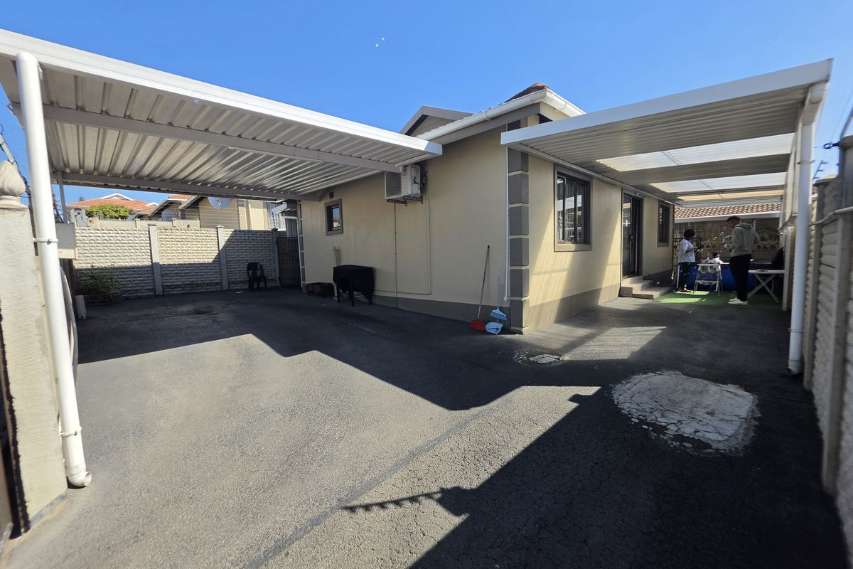 Rear exterior view featuring a paved driveway, dual carports, and perimeter precast concrete walling.
