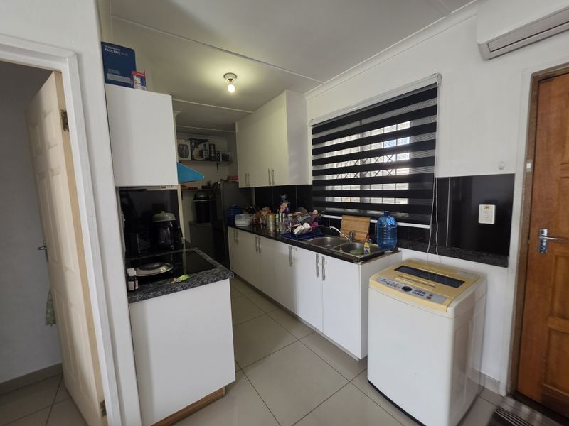 A functional kitchen featuring white cabinetry, dark countertops, tiled flooring, and an integrated electric hob, providing a practical workspace with essential built-in fixtures.