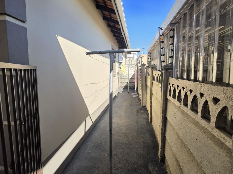 A narrow paved side passage between the house and the boundary wall, featuring precast concrete fencing and integrated electric security wiring.