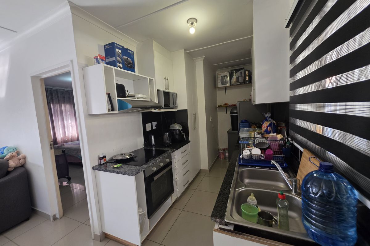 Compact galley-style kitchen featuring granite countertops, built-in oven, electric hob, extractor fan, and double stainless steel sink with tiled flooring.