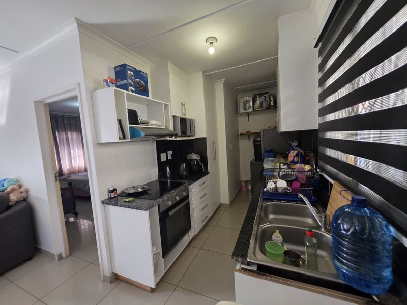 Compact galley-style kitchen featuring granite countertops, built-in oven, electric hob, extractor fan, and double stainless steel sink with tiled flooring.