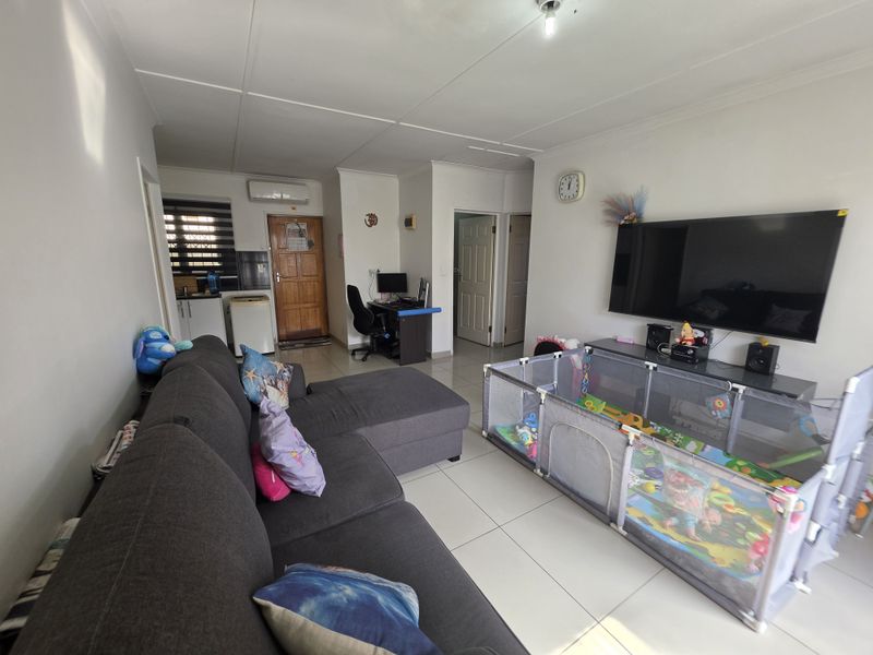 Open-plan living area featuring tiled flooring, coved ceilings, and a wall-mounted air conditioning unit, providing a functional and versatile space.