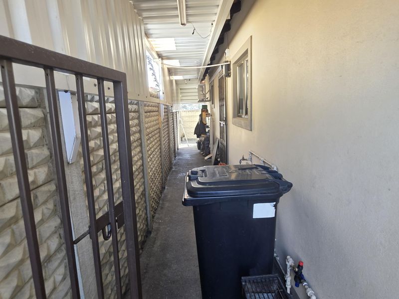 A narrow side utility passage featuring concrete paving, metal roofing, and external plumbing access.