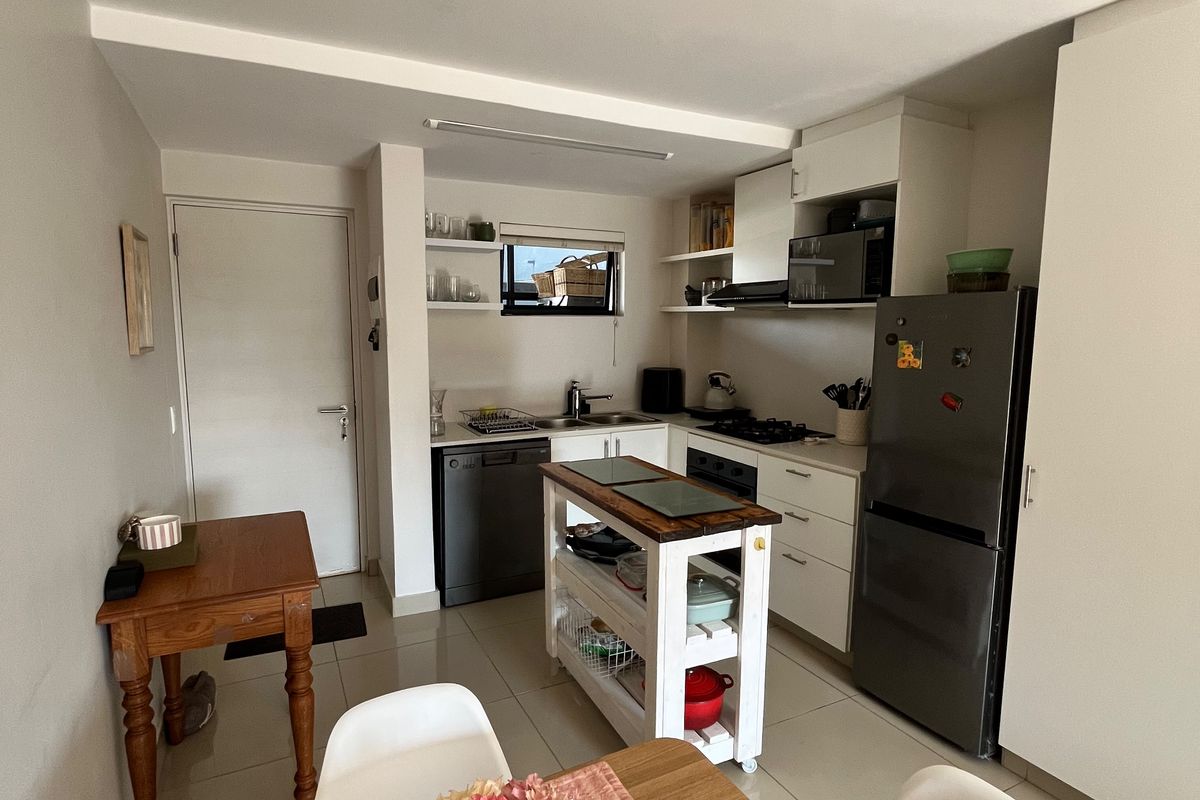 An open-plan kitchen and dining area featuring white cabinetry, tiled flooring, and integrated appliances, providing a functional and well-lit living space.